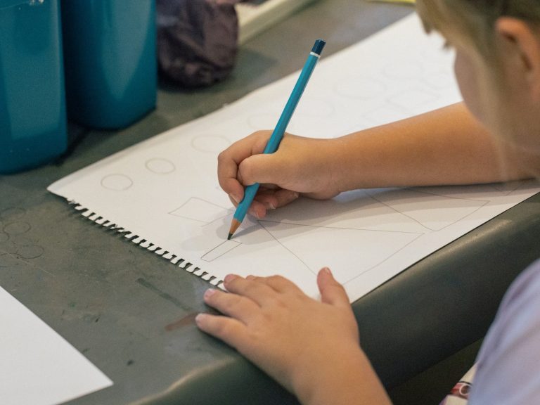 A young person engaged in a visual art activity, drawing on a piece of paper