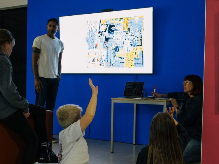 Children are taking part in a workshop, watching images on a projector. One child is raising their hand